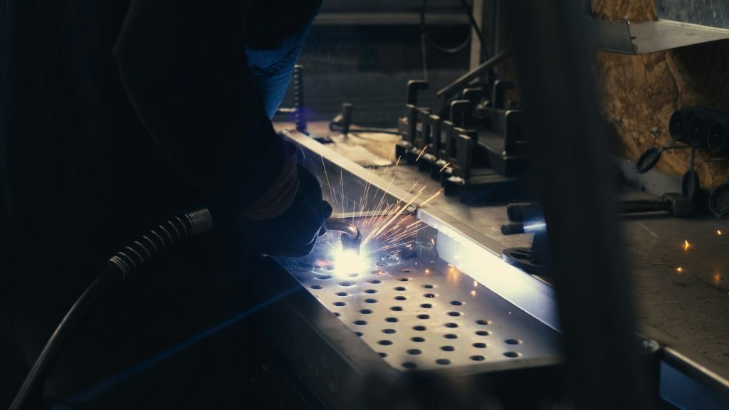 Welder working on a metal sheet with bright sparks in a steel fabrication workshop